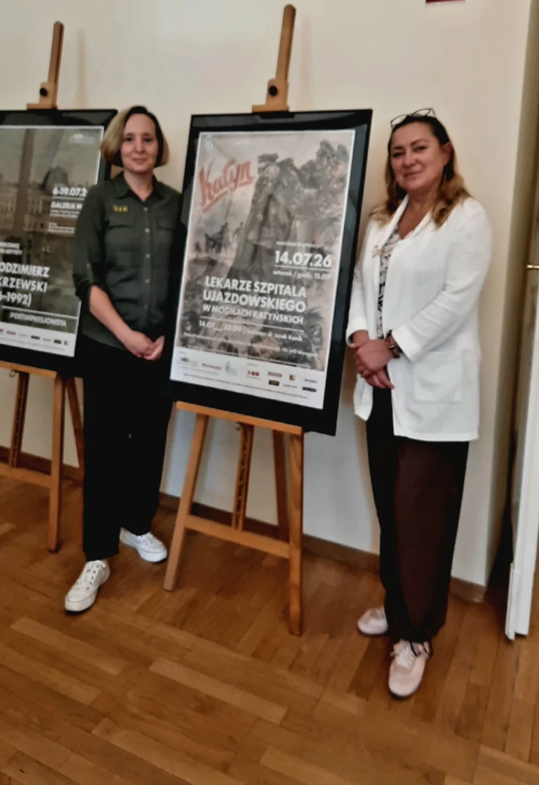 Pracownice DSKM (K. Słojkowska i L. Witkowska) stoją przy plakacie wystawy.