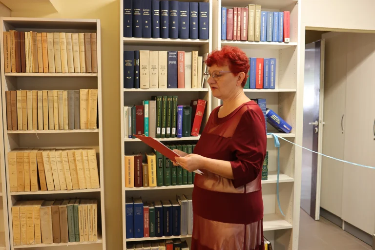 Pani odczytuje tekst. W tle regały biblioteczne.