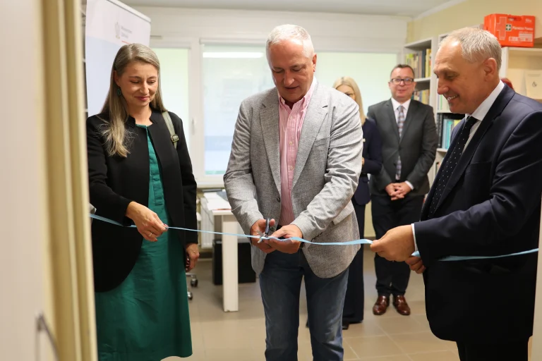 Grupa ludzi stoi przy wstędze. Mężczyzna nacina wstęgę.