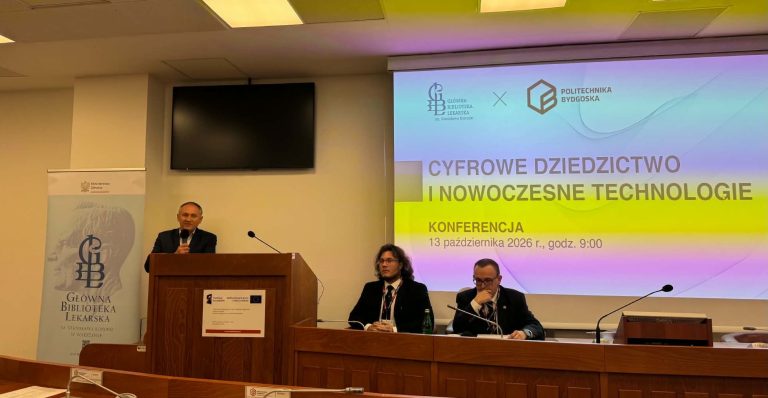 Mężczyzna przemawia przy drewnianej mownicy w sali konferencyjnej. Po jego prawej stronie, przy stole prezydialnym, siedzą dwaj mężczyźni w garniturach. W tle znajduje się ekran projekcyjny z napisem „Cyfrowe Dziedzictwo i Nowoczesne Technologie. Konferencja 13 października 2026 r., godz. 9:00” oraz logo Głównej Biblioteki Lekarskiej i Politechniki Bydgoskiej.