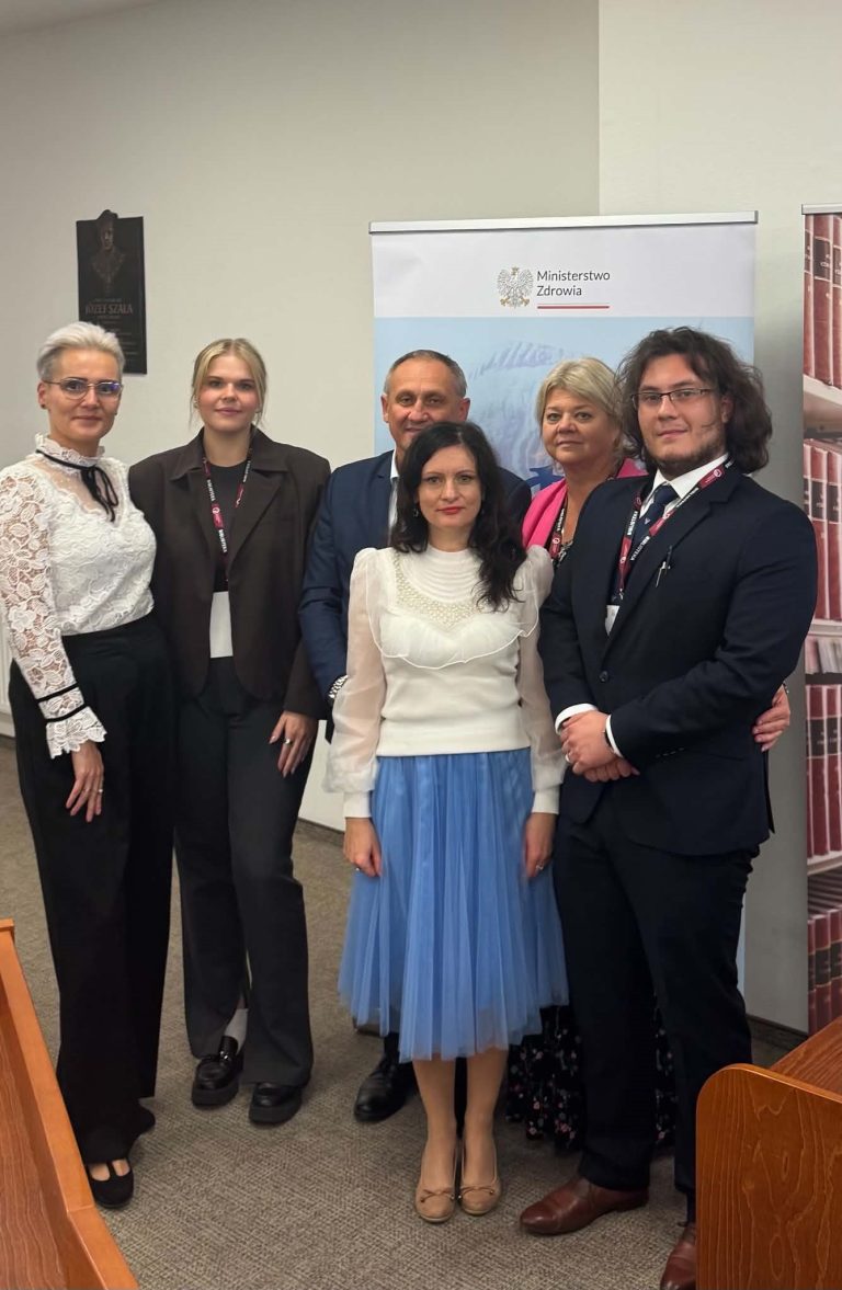 Pamiątkowe zdjęcie grupowe uczestników konferencji stojących obok siebie w sali konferencyjnej na tle ścianki z logo Głównej Biblioteki Lekarskiej.