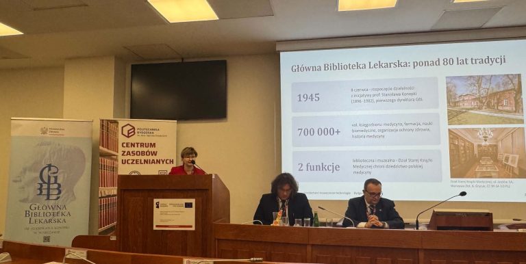 Prelegentka przemawia przy mównicy podczas konferencji. Na ekranie wyświetlany jest slajd dotyczący historii Głównej Biblioteki Lekarskiej z nagłówkiem „Główna Biblioteka Lekarska: ponad 80 lat tradycji” i dwoma zdjęciami budynków. Przy stole prezydialnym siedzą dwaj mężczyźni.