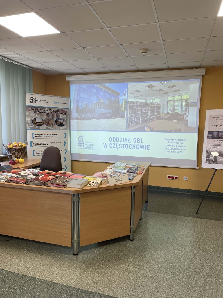 Sala prelekcyjna z ekranem wyświetlającym prezentację Głównej Biblioteki Lekarskiej w Częstochowie oraz stoiskami książkowymi podczas Książkobrania na Politechnice Częstochowskiej.