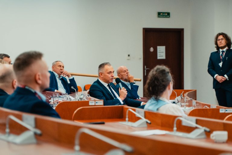 Mężczyzna siedzący w ławce na widowni, wypowiadający się przez mikrofon podczas panelu dyskusyjnego.